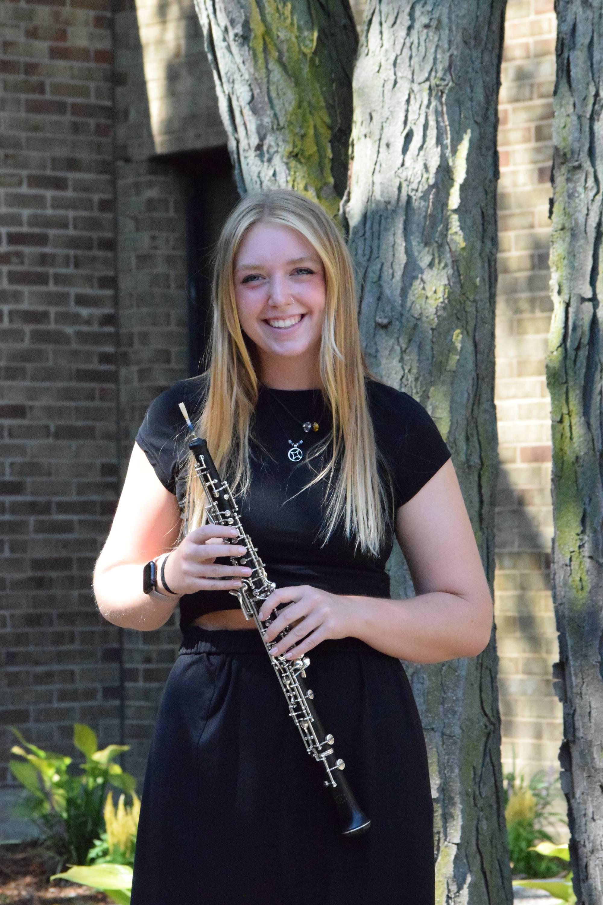 Lauren Schnicke standing outside, holding her oboe and basketball.